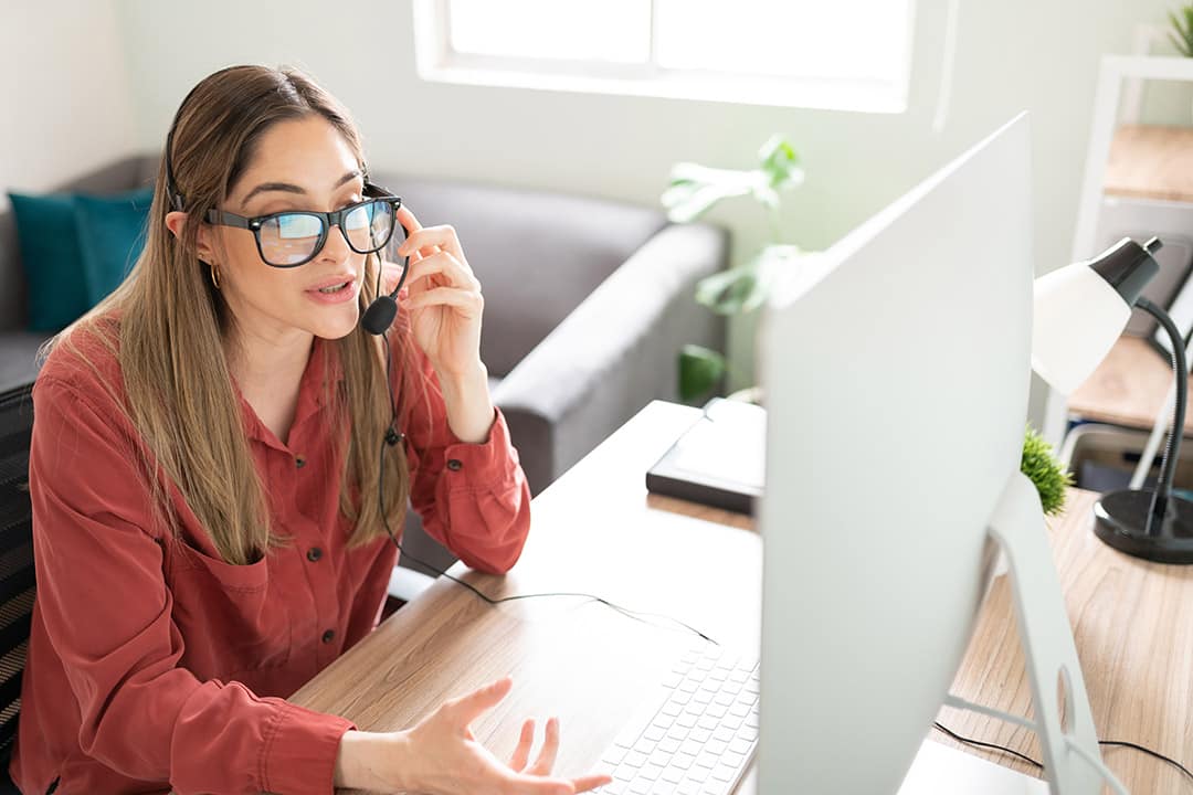 dansk-norsk-tolk Kvinde med headset og briller tolker foran computerskærm i hjemmekontor – illustrerer professionel dansk-norsk tolkning online.